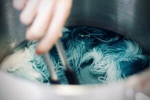 Hand roert lichte strengen zijde in een blauwgroene verfbad