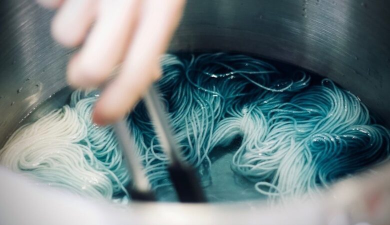 Hand roert lichte strengen zijde in een blauwgroene verfbad