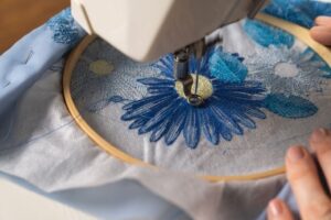 Naaimachine borduurt een blauwe bloem in een houten borduurring