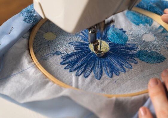 Naaimachine borduurt een blauwe bloem in een houten borduurring